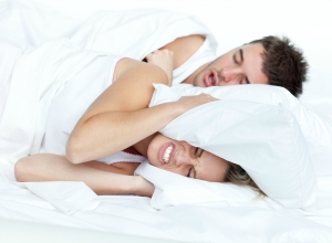 woman scowls with head under pillow to block mans snoring in bed woman scowls with head under pillow to block mans snoring in bed